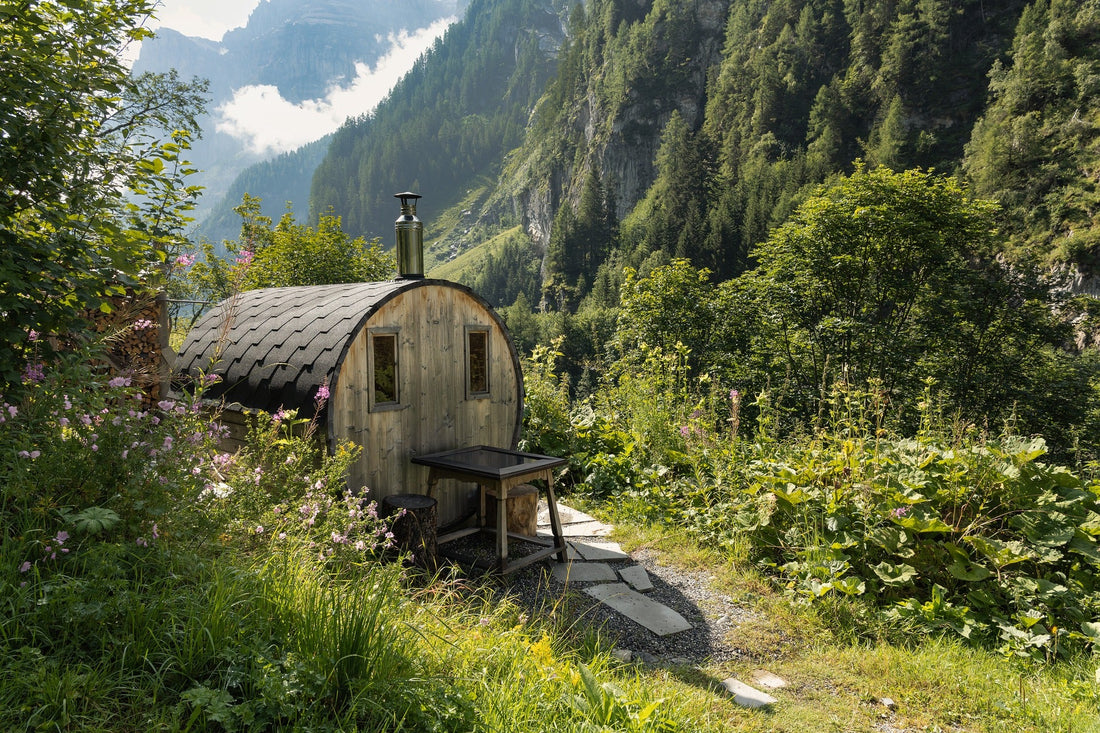 Small wooden sauna in a forest with outdoor table.