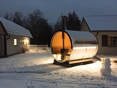 Barrel sauna in a snowy environment with interior lighting.