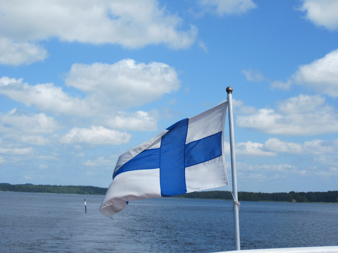 Finnish flag on a flagpole with a lake in the background.