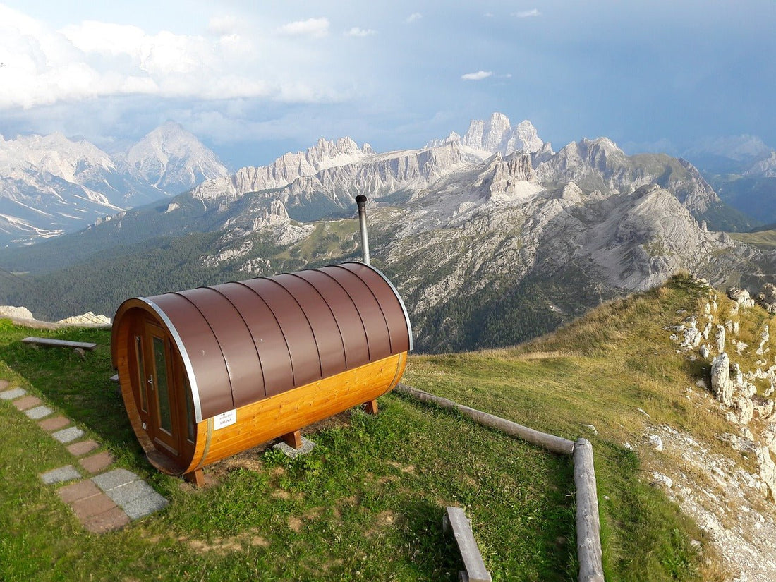 Barrel sauna on a hill with mountains in the background.