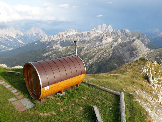 Barrel sauna on a hill with mountains in the background.