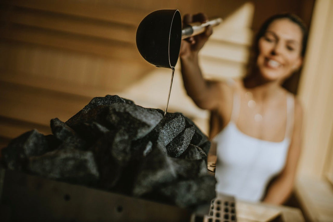 Woman pouring water on the hot stones in the sauna.