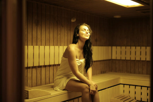 Woman sitting on a sauna bench, covered by a towel.