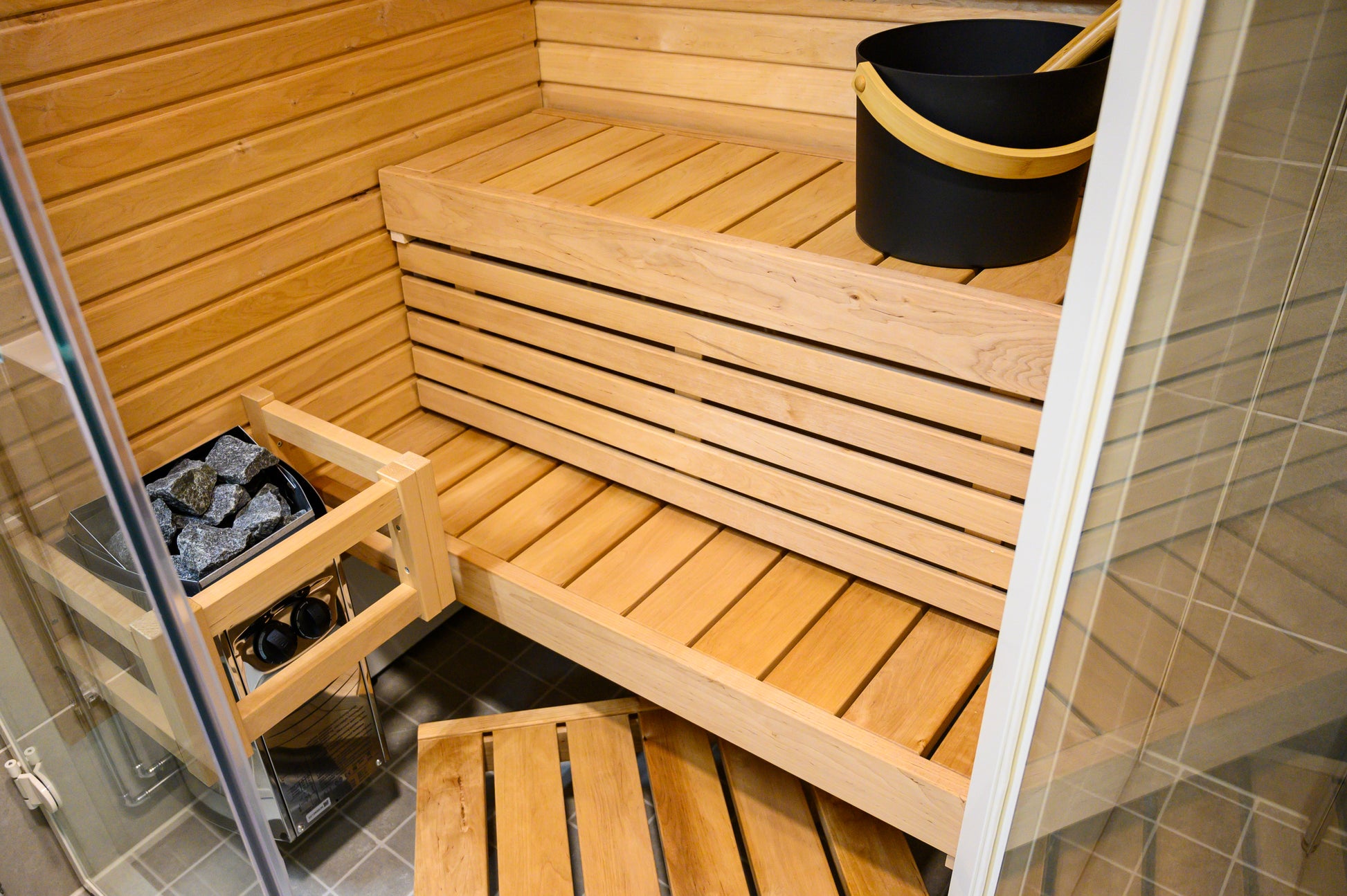 Sirius Corner sauna with wooden benches and black bucket.