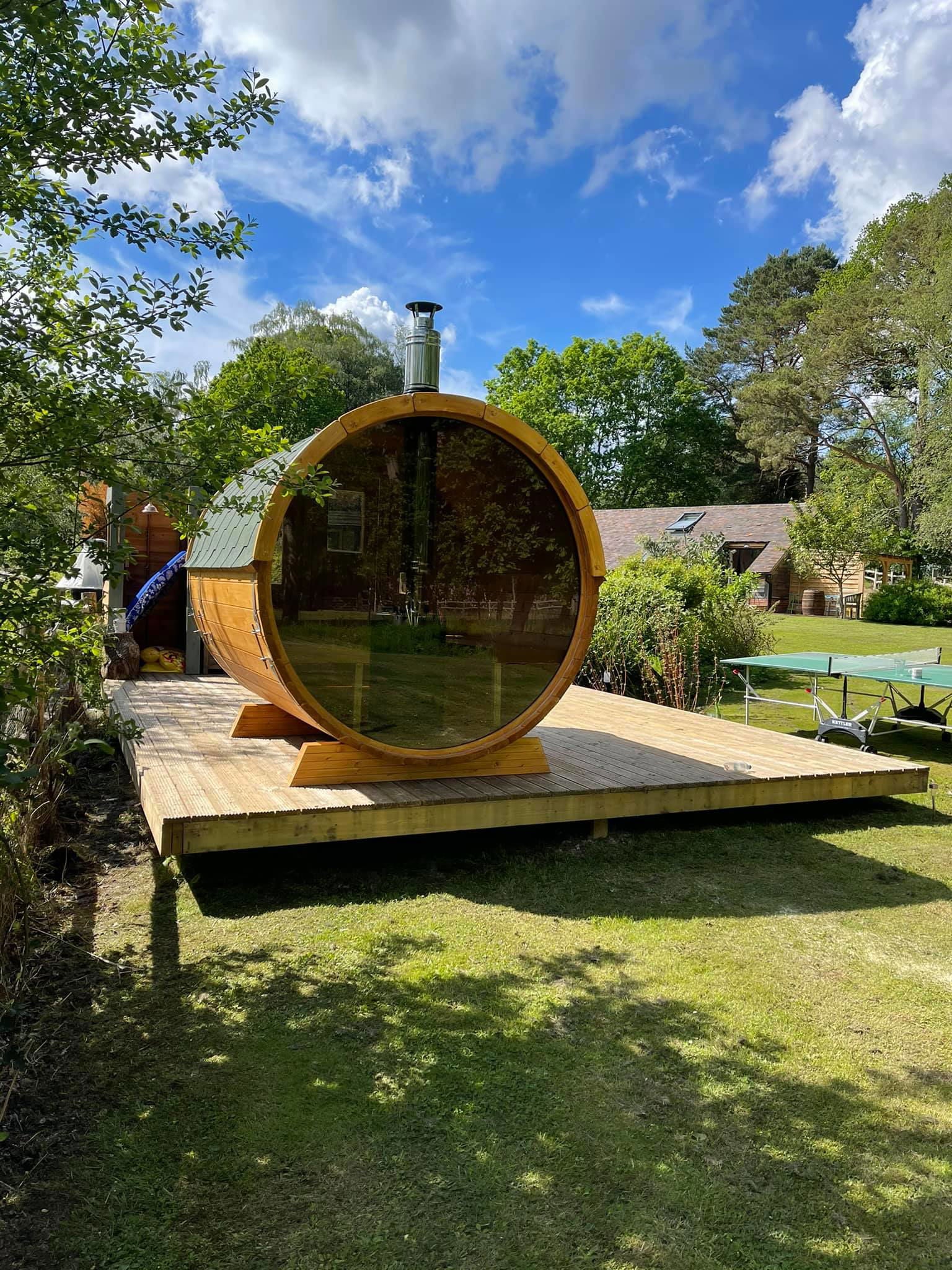 Outdoor sauna Saunamo Barrel 250 with glass wall on wooden deck.